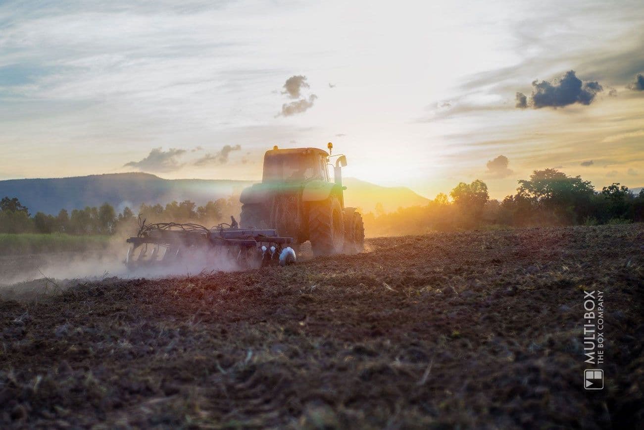 Traktor pflügt ein Feld bei Sonnenuntergang, aufgewirbelte Erde und Staub in ländlicher Umgebung. Landwirtschaft, Agrartechnik, nachhaltige Bodenbearbeitung.