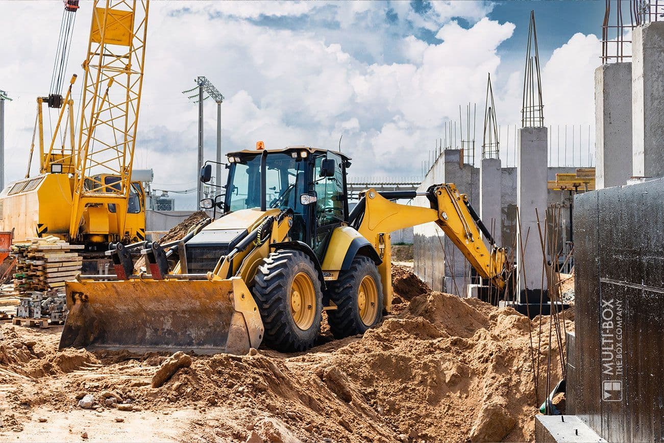 An excavator in operation on a construction site, surrounded by construction machinery and scaffolding.
