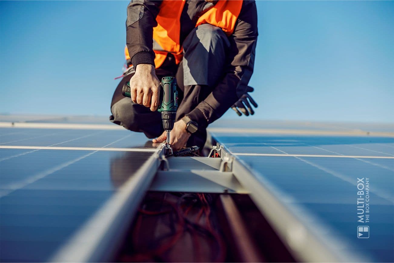 A technician screws a solar panel onto a roof using a drill.