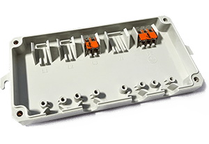 Ein Kunststoffgehäuse mit vorgefertigten Aussparungen für Steckverbinder und Komponenten. Zwei orange Steckverbinder sind sichtbar