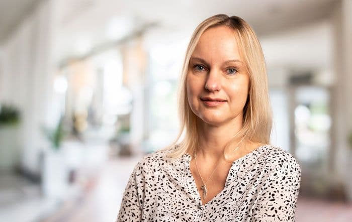 Eine junge, lächelnde, blonde Frau in einem hellen und sommerlichen Oberteil.
